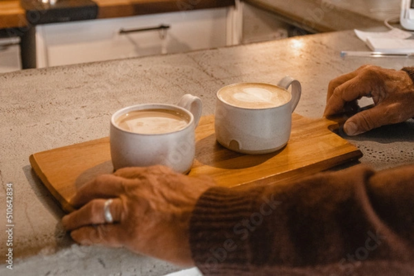 Fototapeta Old man's hands picking up wooden platter with two coffees
