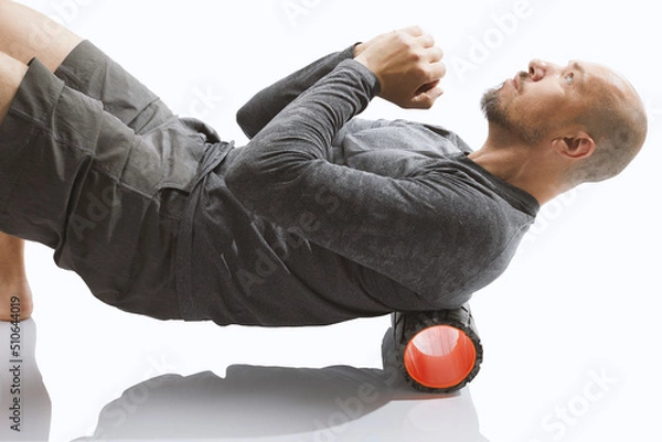 Obraz Close-up  roller for body massage. Bald guy doing an exercise  with foam roller on his upper back against white background.