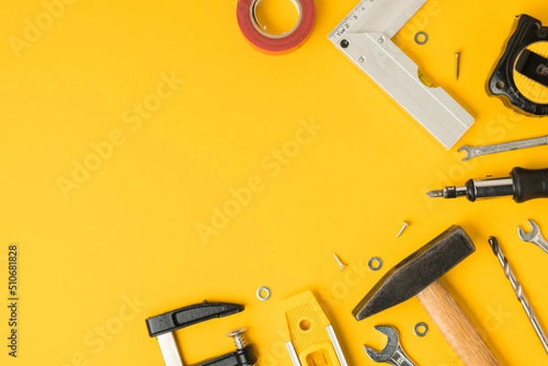 Fototapeta Handyman's tools. Flat lay of clamps, wrench, screwdriver, drill, angle, bubble level and tape measure on yellow background. Happy Father's Day. Free space  for you text