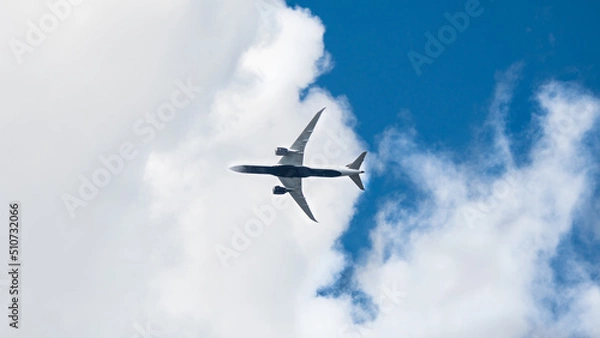 Fototapeta Passenger airplane flying overhead. Modern airliner taking off and landing background with copy space. Blue sky and white clouds