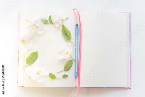 Fototapeta Open book with white sheets and a blue pen in apple blossoms around