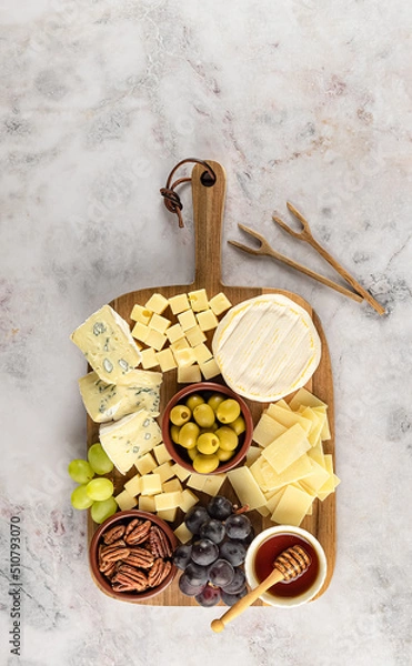 Fototapeta Party cheese board with a variety of cheese, grape, nuts, olives, and honey on a kitchen plate