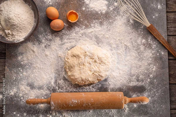 Fototapeta Ready to be baked dough. Top view of board, rolling pin and flour and dough.