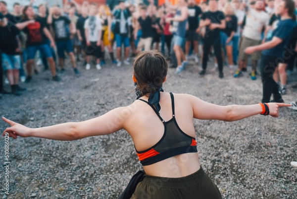 Obraz People at summer metal music festival before the mosh pit. Girl with hands raised wide show the right moment to start
