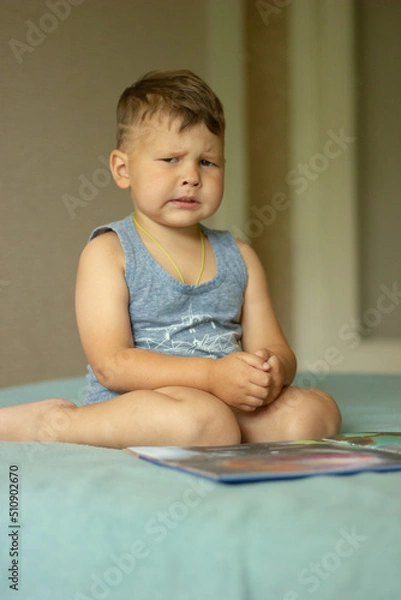 Fototapeta The boy sitting on the bed shows emotionally that he is unhappy and sad