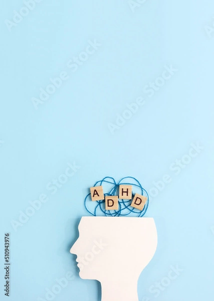 Fototapeta Silhouette of human head and wooden blocks with the lettering ADHD on blue background. Minimal concept of attention deficit hyperactivity syndrome. Vertical banner, copy space