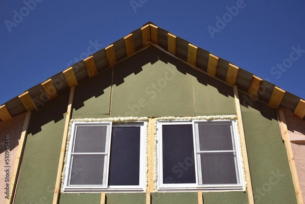Fototapeta Wall covering of the frame house with panels of vinyl siding. construction or reconstruction, repair of the house. Installation of plastic Windows in a new residential building on blue sky background.