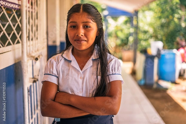 Fototapeta Nicaraguan elementary student girl smiling and looking at the camera with her arms crossed in a school in the rural area of Masaya