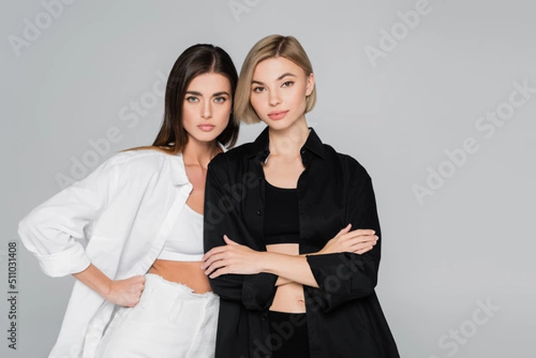 Fototapeta women in black and white shirts standing with hand on hip and crossed arms isolated on grey.