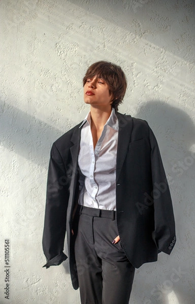 Fototapeta Young thoughtful and sad business woman on background of wall in sun rays, portrait girl in classic suit