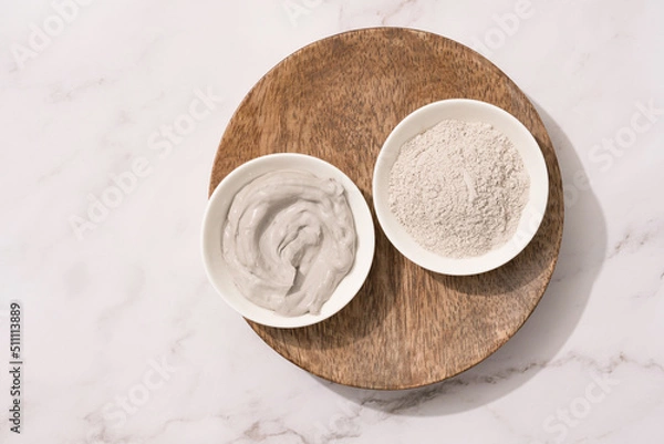 Obraz Bowl with gray cosmetic clay cream and clay powder on wooden tray - mineral bentonite facial mask. Skincare beauty concept. Selective focus. Top view