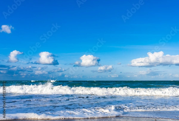 Fototapeta Blue waves wash over a beautiful beach in Melbourne Beach. Blue sky with white clouds. Atlantic Ocean at sunset in Florida in winter.