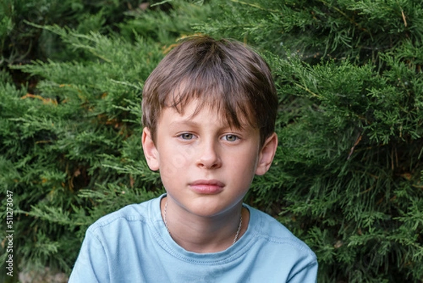 Fototapeta A 9-year-old boy looks intently into the camera. Portrait of a white Eastern European boy in nature
