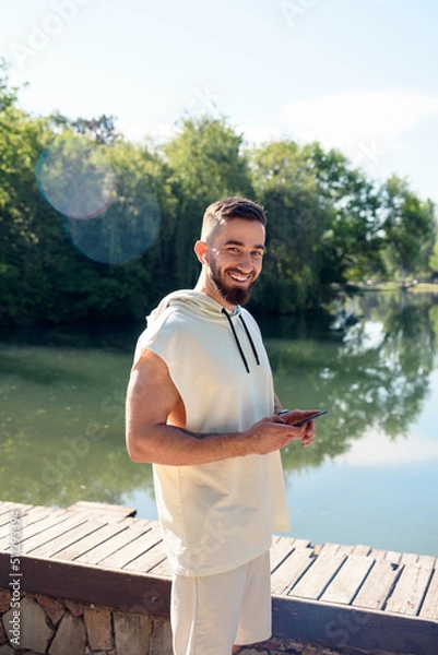 Obraz Young handsome men look at camera taking phone with his hand listening music with headphones smiling