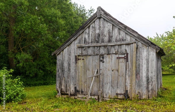 Obraz Looking across the green grass at an old black wooden barn building with closed doors