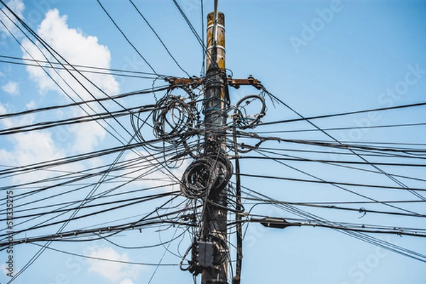 Fototapeta Cable or wire chaos and splice or termination box with fiber optics on a concrete pillar creating a connection confusion of a network infrastructure against blue sky