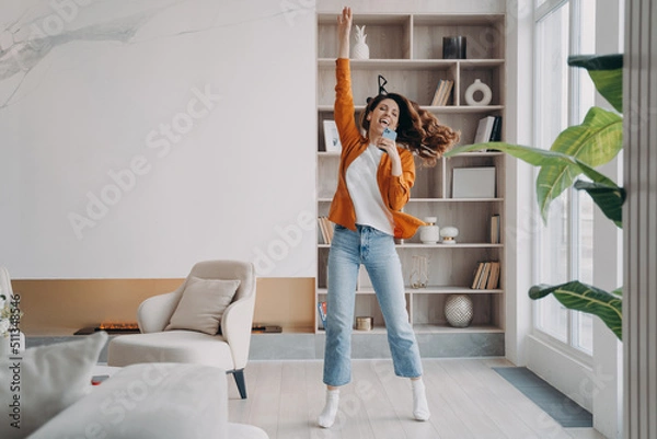 Fototapeta Young woman is singing, dancing and jumping. Girl having fun crazy and screaming at home.