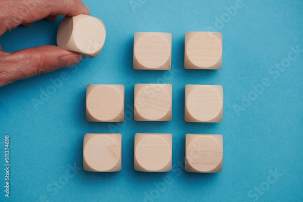 Fototapeta Nine wooden cubes on a blue background standing on top of each other in three rows. The fwmale hand adds the upper left cube, free space for letters, numbers, symbols