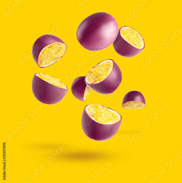 Fototapeta Passion fruit. Pieces of flying fruit. Purple fruits with yellow seeds flying in the air, isolated on a yellow background.