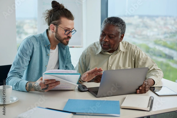 Obraz An educator patiently explaining to an african senior student how to solve a programming problem.