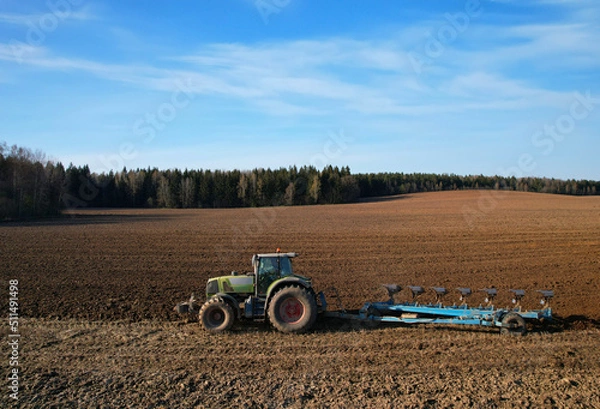 Fototapeta Tractor plow soil cultivating. Green Tractor plowing field. Cultivated land and soil tillage. Agricultural tractor on farm field cultivation. Tractor disk harrow plowing farm field. .