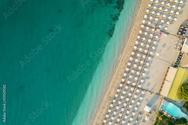 Fototapeta Aerial view of many white sunbed, lounge, umbrellas on sandy beach. Summer and travel concept. Blue, turquoise transparent water surface of ocean, sea, lagoon. Aerial, drone view