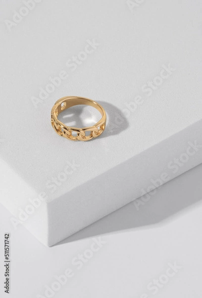 Fototapeta Vertical shot of chain shape golden ring on white podium with copy space