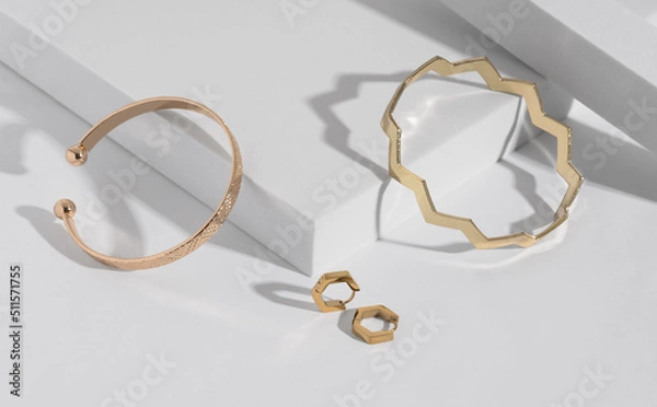 Fototapeta Two modern geometric shape golden bracelets and earrings pair on white podium with copy space