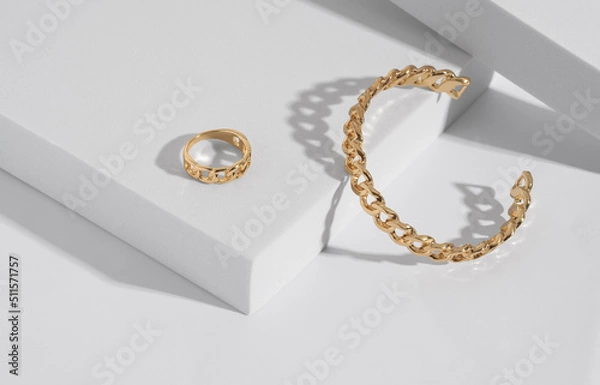 Fototapeta Chain shape golden modern bracelet and ring on white podium with copy space