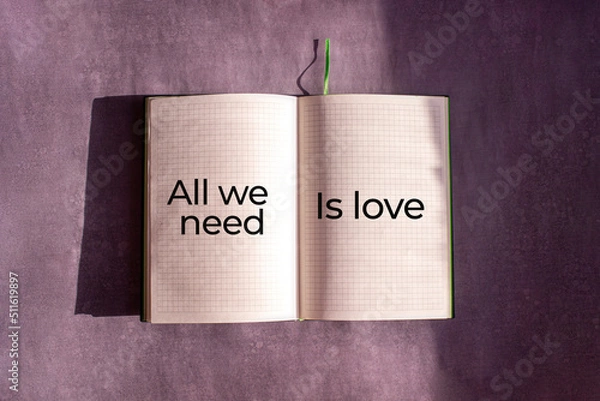 Fototapeta An open notebook is on the gray background. The word "All we nedd is love" is written on a blank sheet of notebook. Learning, education concept.
