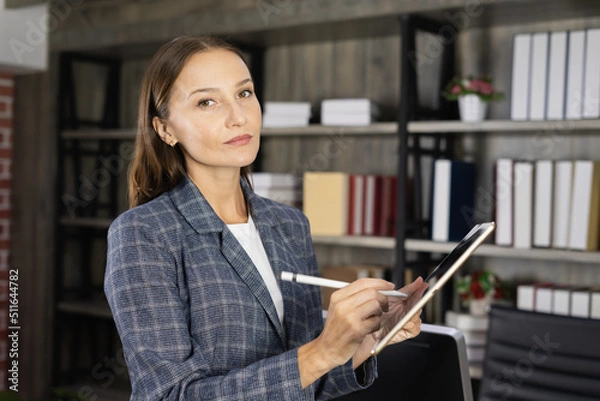 Obraz young woman writing on tablet, wearing suit and looking at camera in workplace. beautiful young woman look as businesswoman or worker or secretary working business in corporate office