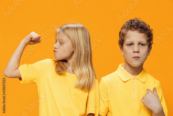 Fototapeta funny, funny school-age children stand on a yellow background in yellow clothes and show muscles to each other
