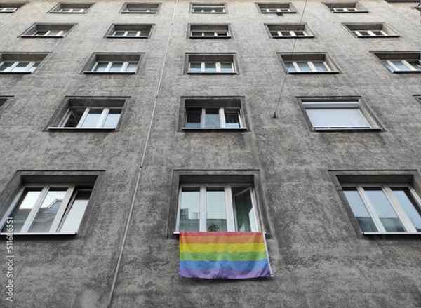 Fototapeta Pride month rainbow colored flag hanging from a window in the street