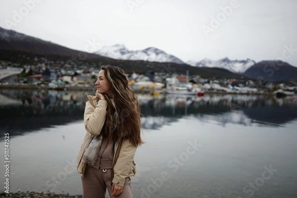 Fototapeta In the photo, a beautiful girl against the background of the city of Ushuaia, with houses of Argentine architecture and a beautiful view of the lake.