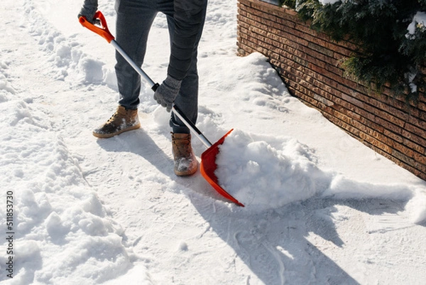 Fototapeta Close-up of a man cleaning and clearing snow in front of the house on a sunny and frosty day. Cleaning the street from snow on a winter day. Snowfall, and a severe snowstorm in winter.