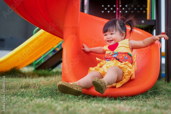 Fototapeta Asian cute baby playing on a slide at playground. 1 year 6 month baby enjoy and laugh at playground use as concept of play, health, mood and motion of baby and kid development.