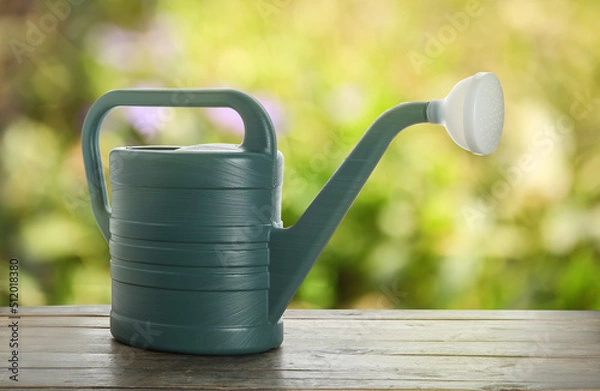 Fototapeta Watering can on wooden table outdoors