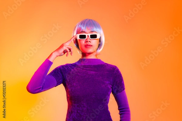 Fototapeta Young asian girl in purple sweatshirt silver and blue color short hair style wearing sunglasses posing thinking like robot on the orange and yellow background. Metaverse and future concept.