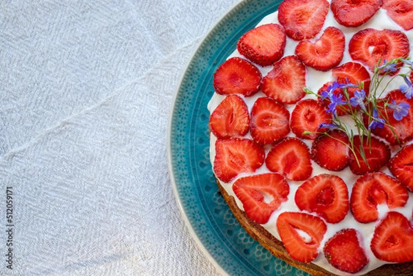 Fototapeta Cake with strawberries and cream on blue plate. Summer Strawberry and Cream sponge Layer Cake on white table cloth background. Top view, copy space. Midsummer food dessert