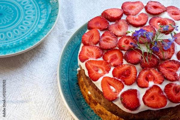 Fototapeta Cake with strawberries and cream on blue plate. Summer Strawberry and Cream sponge Layer Cake on white table cloth background. Top view, copy space. Midsummer food dessert