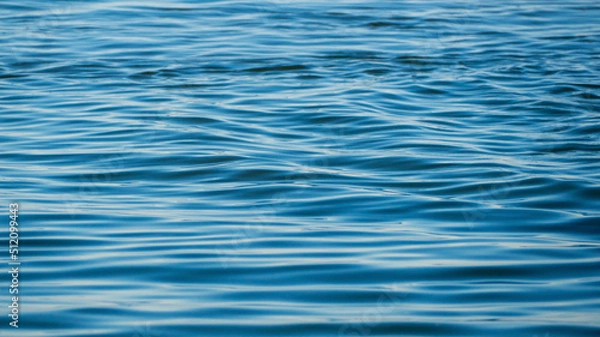 Fototapeta Blue sea water with calm ripples close-up, texture background. Texture of the sea surface for a natural water background. Background texture of waves on a blue ocean on a sunny day