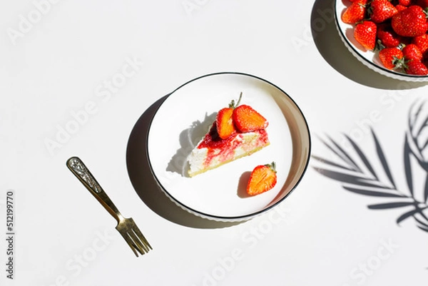 Fototapeta Cheesecake with strawberry jam and fresh strawberry on light background in sunlight with palm leaves shadows. Minimalist creative composition.