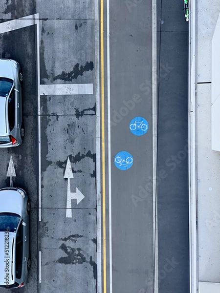 Fototapeta A picture from above from a road with a pre-sorting area with two cars in it, a second empty pre-sorting area with two arrows, a bike path with two blue circles with a bike in it and a walkway