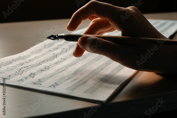 Obraz Woman's hand with a pen drawing notes in a music book, writing a melody by hand, composing music