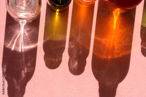 Fototapeta Different cosmetic glass bottles standing on pink background. Abstract pattern by shadows and reflections in the sunlight. Red, green and yellow shades. Flat lay style with copy space