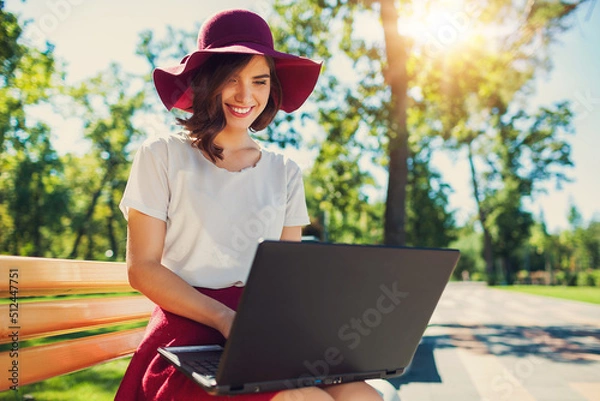 Fototapeta Girl with a laptop on a bench in the park in summer