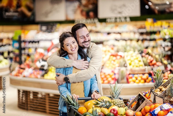 Fototapeta A couple in love hugging in supermarket while purchasing in supermarket.