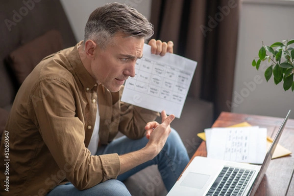 Fototapeta Man sitting showing document on laptop screen