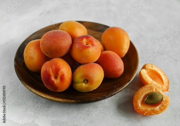 Fototapeta Fresh ripe apricots in a wooden bowl on a table made of natural marble.  Apricots are rich in vitamins and minerals, such as: vitamin A, beta-carotene, vitamin C, potassium, silicon, cobalt