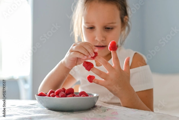 Fototapeta The little girl played with raspberries on her fingers
